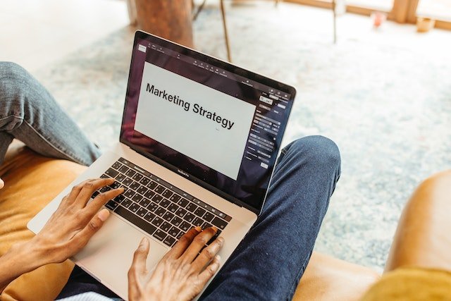 A Person Typing on a Laptop with Marketing Strategy Written Accross the Screen