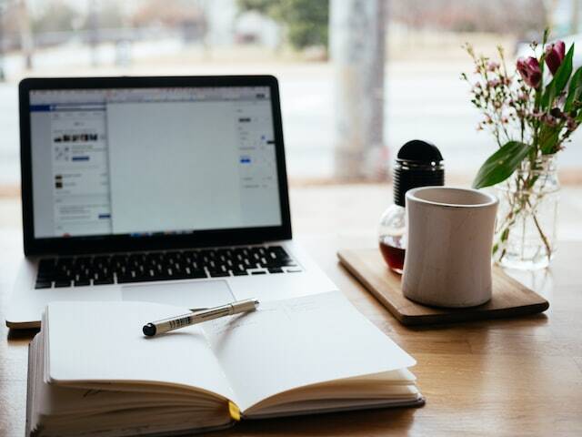 desk set up with a laptop open notebook and pen and coffee cup